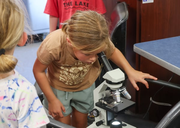A young camper looks into a laboratory microscope during a healthcare camp activity.