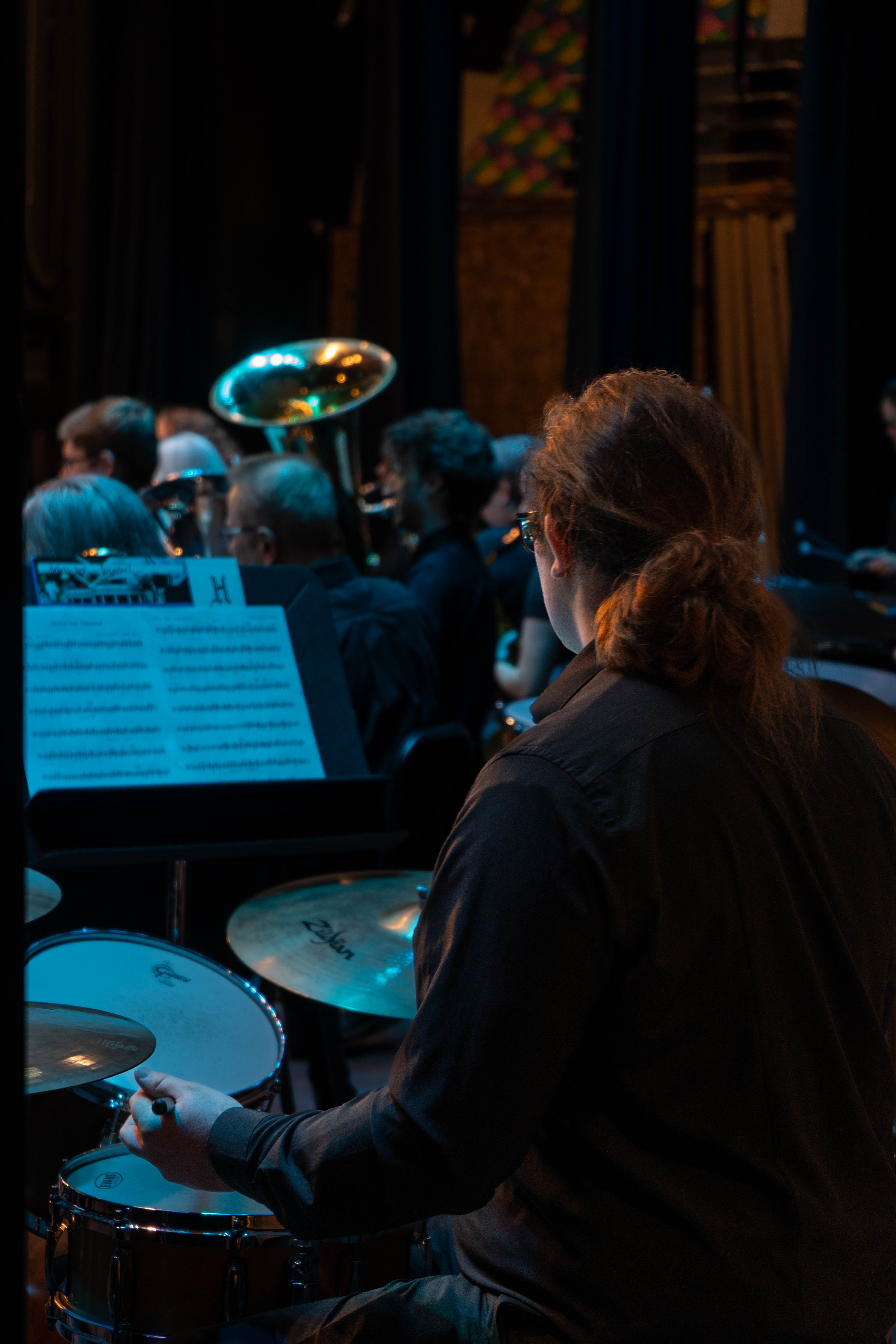 A percussionist plays the drums during the 2026 Spring Concert: Chiaroscuro. Viewed from behind, the musician focuses on their sheet music while other members of the Rend Lake College concert band perform under blue stage lighting.