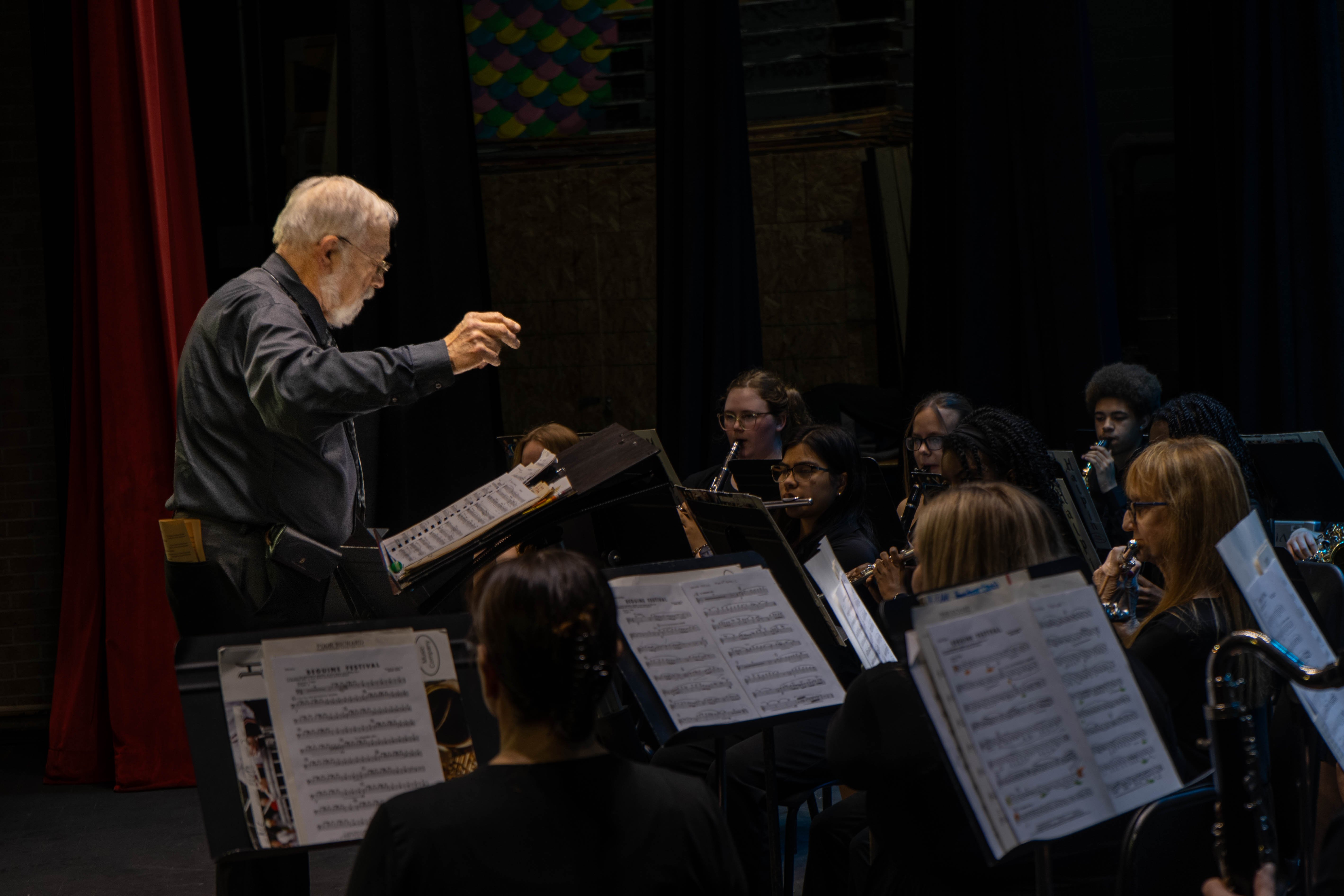 Conductor William Reynolds leads the Rend Lake College concert band during the 2026 Spring Concert: Chiaroscuro. Musicians playing woodwind instruments, including flutes and clarinets, follow his direction from behind their music stands on the RLC Theatre stage.