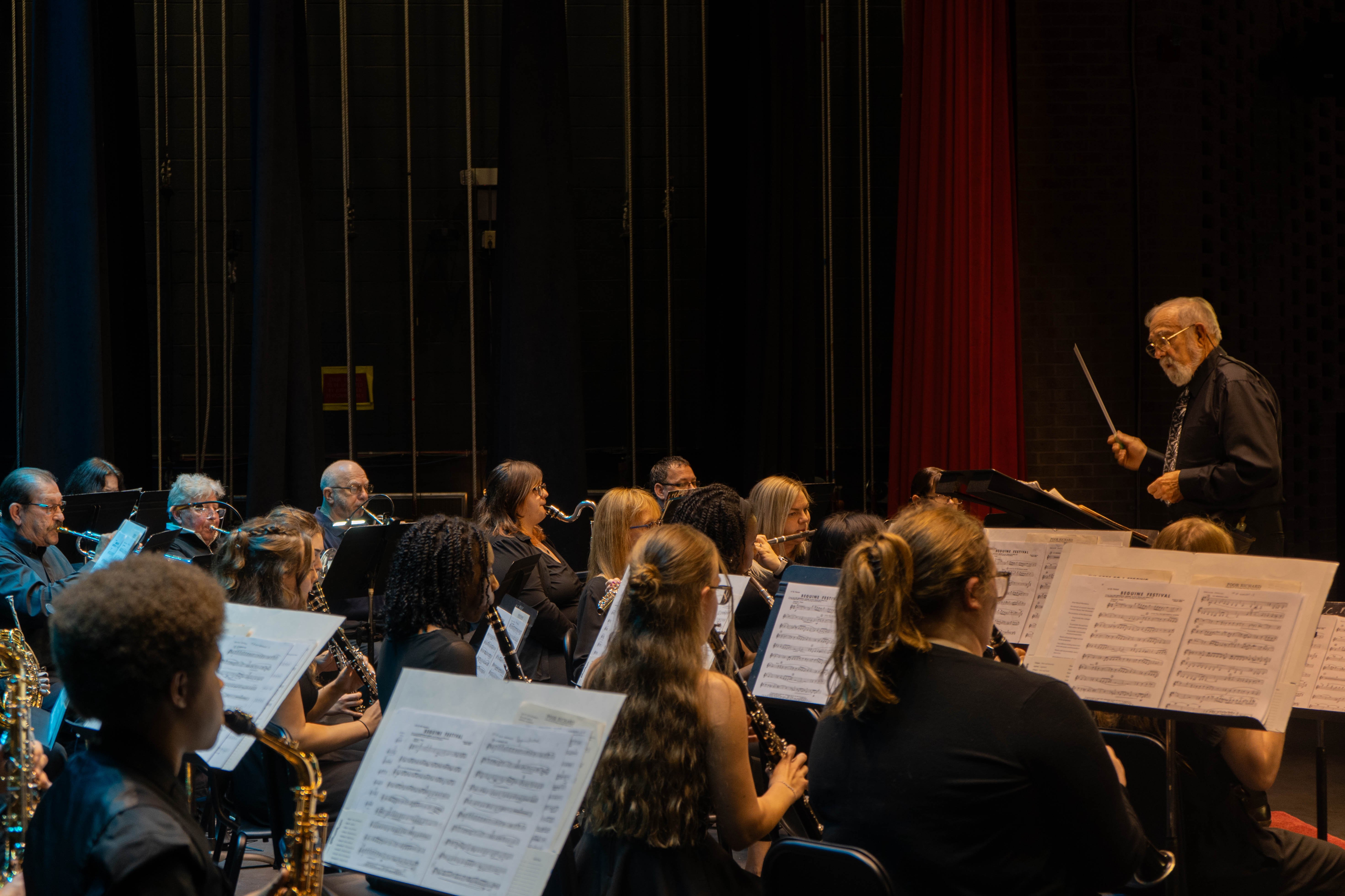  Conductor William Reynolds leads the Rend Lake College concert band from the side of the stage during the 2026 Spring Concert: Chiaroscuro. The musicians, including those playing saxophones and clarinets, are seated with their sheet music in the foreground.