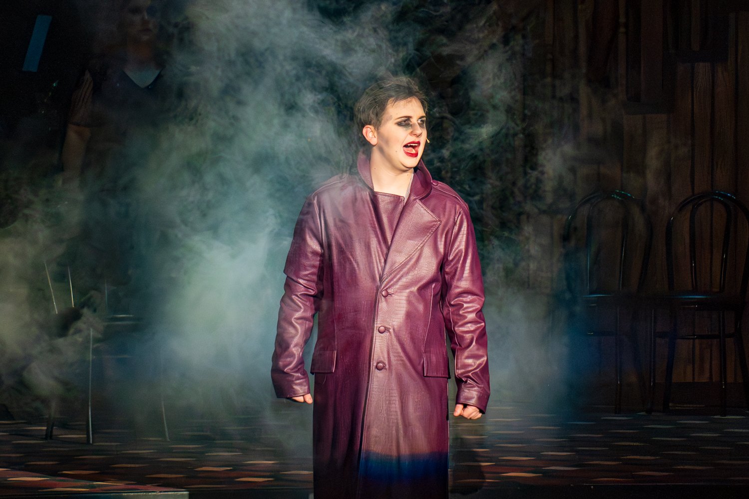 Holdyn Westberry as the Emcee from Cabaret stands center stage, partially obscured by a thick haze of stage fog.