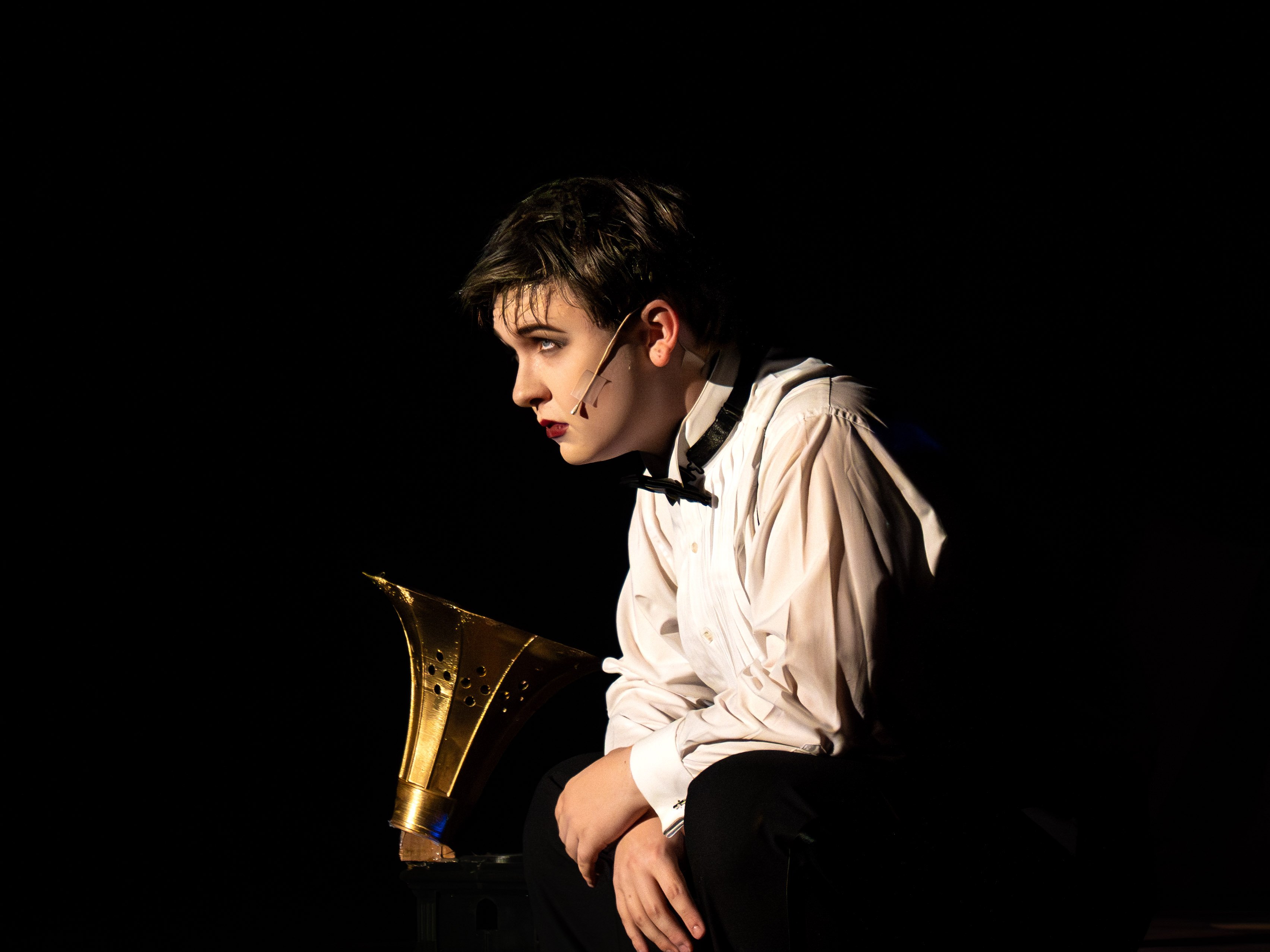 Holdyn Westberry as the Emcee from Cabaret is captured in a somber, profile view against a stark black background.