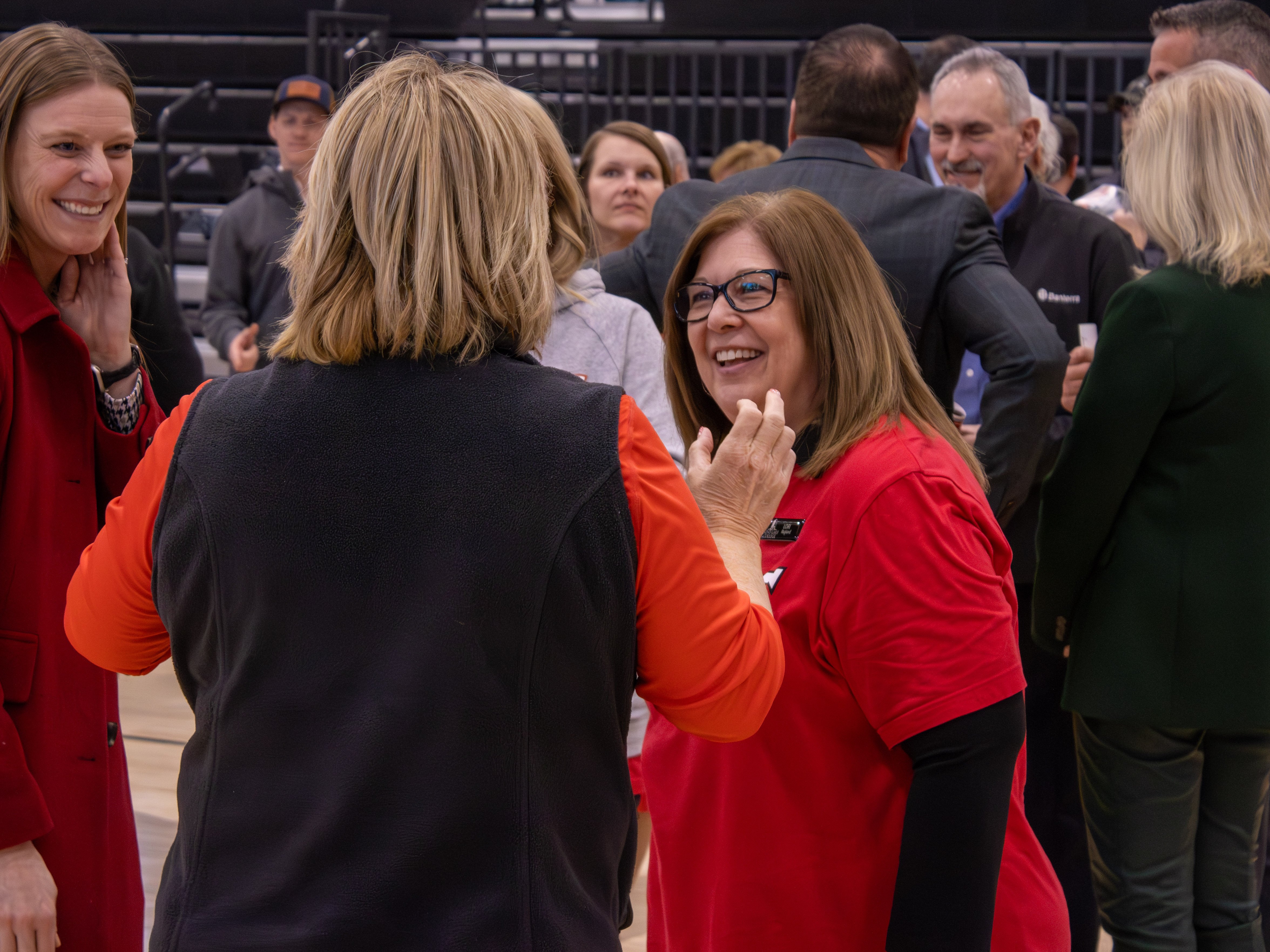 President Lori Ragland (center-right, facing left) smiles while talking with Terri Bryant (left, in a red coat) on the gym floor following the ceremony.