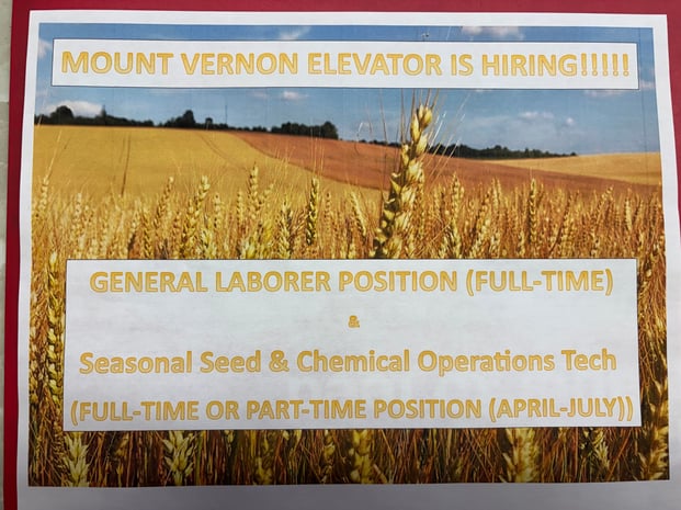 A printed hiring flyer with a background image of a golden wheat field under a blue sky. At the top, large yellow text reads, “MOUNT VERNON ELEVATOR IS HIRING!!!!!” Below, in a white box with yellow lettering, it lists open positions: “GENERAL LABORER POSITION (FULL-TIME)” and “Seasonal Seed & Chemical Operations Tech (FULL-TIME OR PART-TIME POSITION (APRIL–JULY)).”