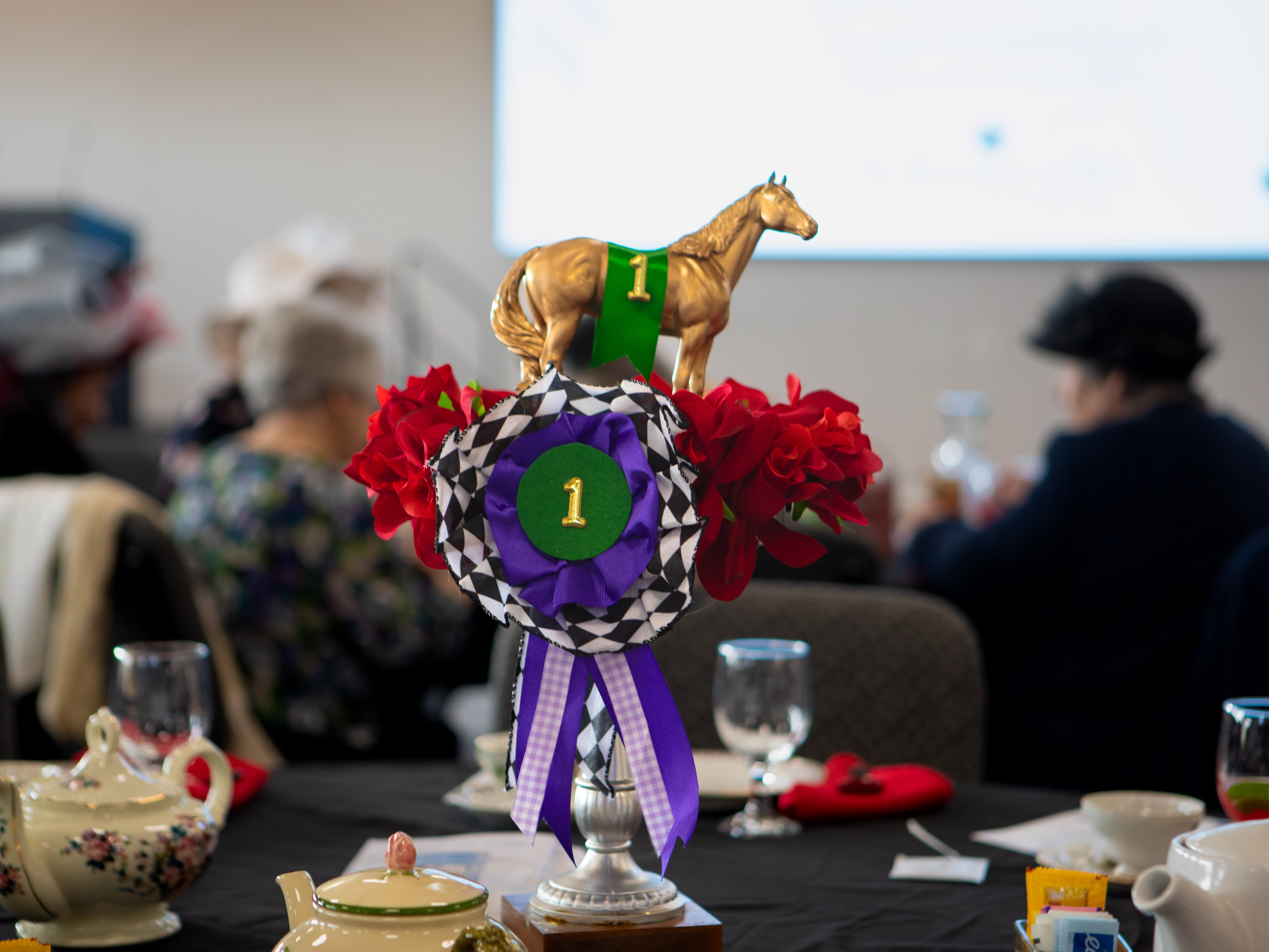 A Kentucky Derby-themed centerpiece sits on a table, featuring a gold horse figurine standing atop a bed of red roses.
