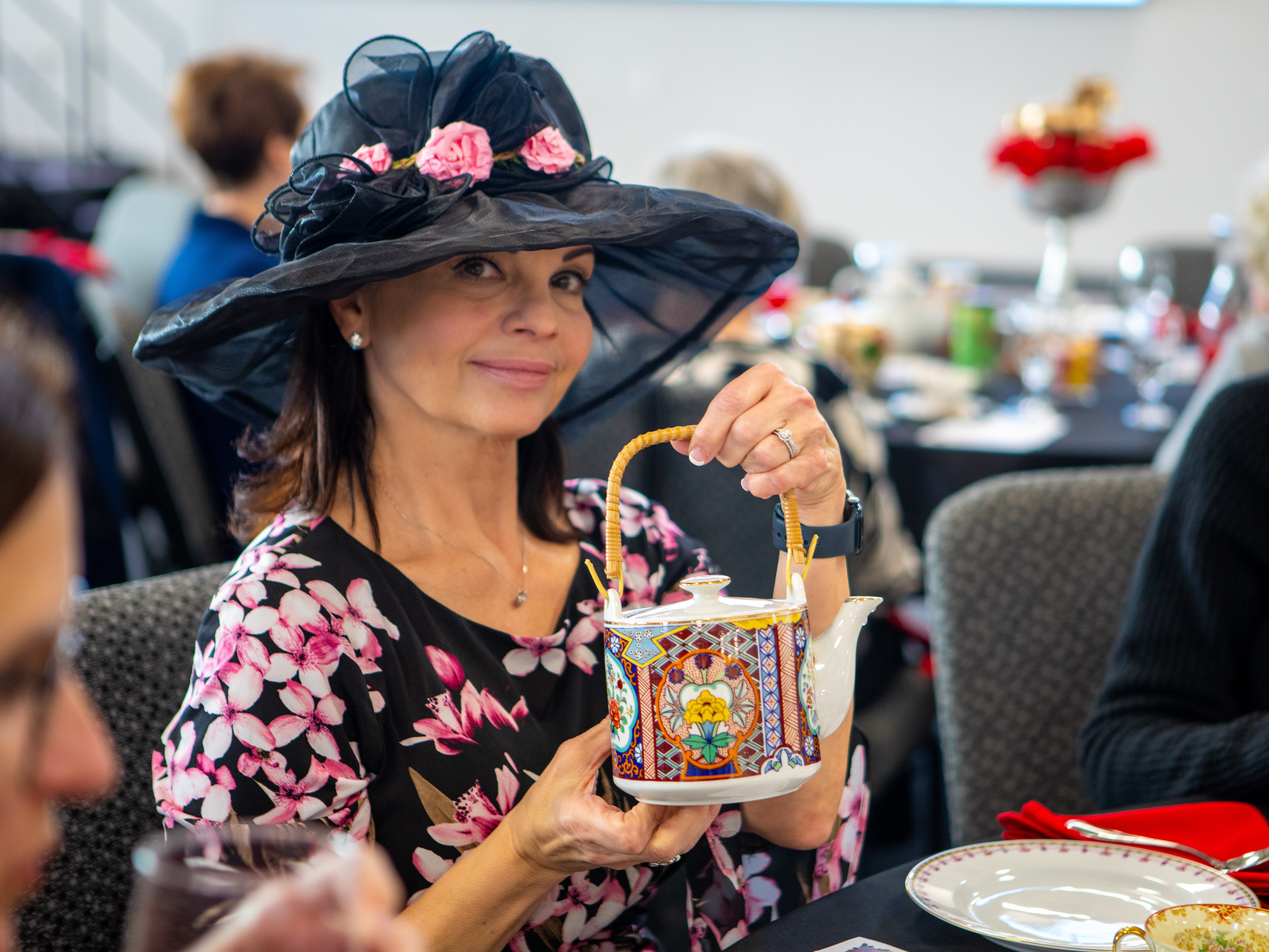 RLC's Tracey Webb smiles at the camera while holding up a colorful, intricately patterned teapot with a bamboo handle.