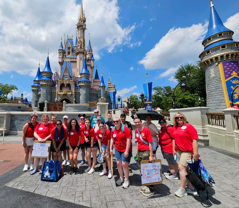 A group of Rend Lake College STARS students and staff wearing matching red shirts pose together in front of Cinderella Castle during their 2024 trip to Disney World.